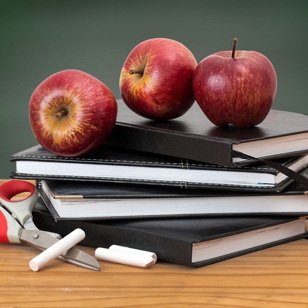 Red apples on top of a stack of books with scissors and chalk next to them